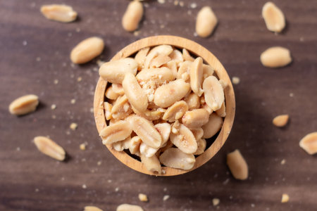 Peanuts in a wooden cup rest on a natural wood floor, creating a warm and rustic food-themed scene,...