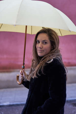 close-up of a pretty girl on the street with a yellow umbrella looking at cameraの写真素材