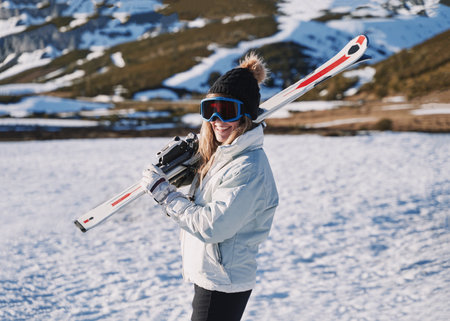 pretty girl smiles while carrying some skis in the snow. girl in a hat and goggles.の写真素材