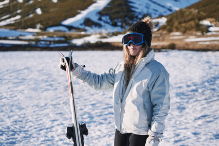 stylish pretty girl waits on the mountain with her skis and equipped with goggles and hat.の写真素材