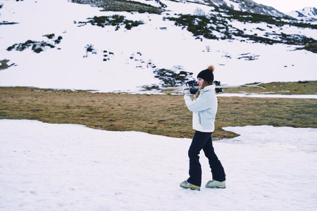 pretty girl carries ski equipment on her shoulder while moving down the mountain. side view with copy spaceの写真素材