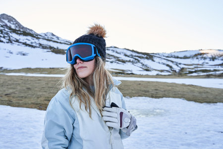 beautiful girl poses before the camera with a casual and calm appearance equipped with a hat and snow goggles in the mountainの写真素材