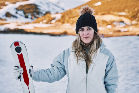 pretty girl holds some skis while looking at the camera with a slight smile in the mountainの写真素材