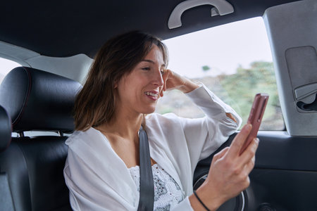 pretty girl surfs the internet with her mobile while smiling inside a car on a rainy dayの写真素材