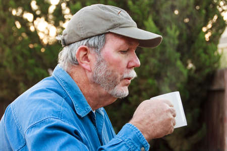 Senior blowing steam from hot drinkの写真素材