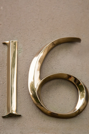 Arabic numbers sixteen in beveled brass on a white backgroundの写真素材