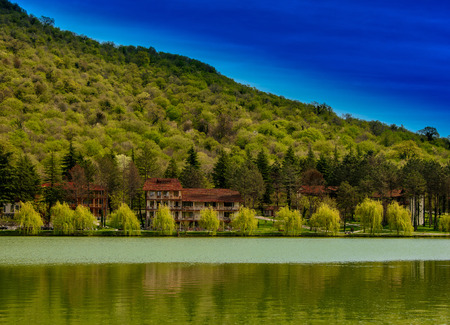 Tranquil lake vista with houses, mountain and blue skiesの写真素材