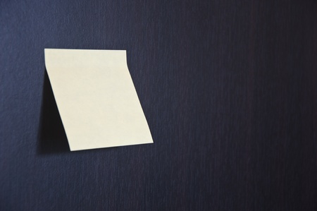 Blank Yellow Sticky Note stuck on the black wooden walls. Studio shot.の写真素材