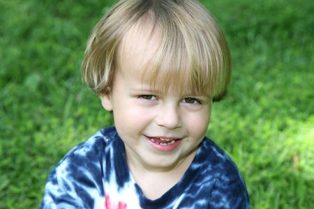 Cute 3 year old boy sitting in the grass looking up.
