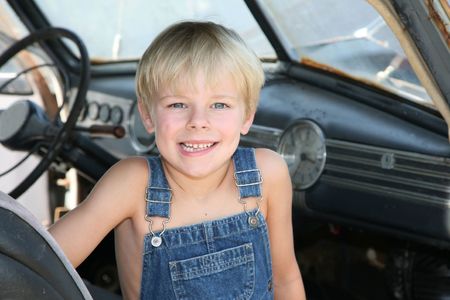 Young boy sitting in an antique car wearig old overallsの写真素材