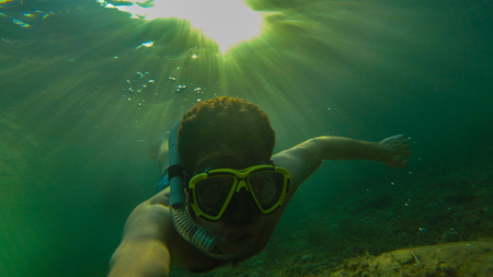 man diving inside the water making snorkling with the sun on the back with blue and green colorsの写真素材