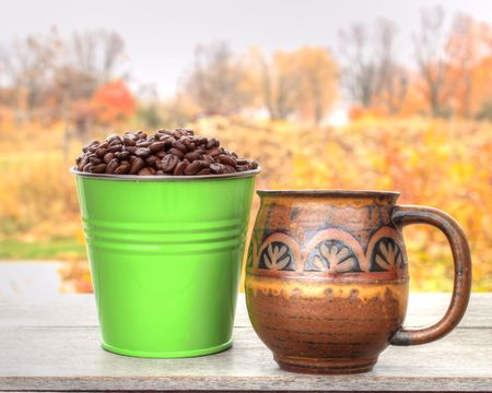 Fresh coffee beans in colorful green bucket with coffee cup set in an outdoor Autumn scene.の写真素材