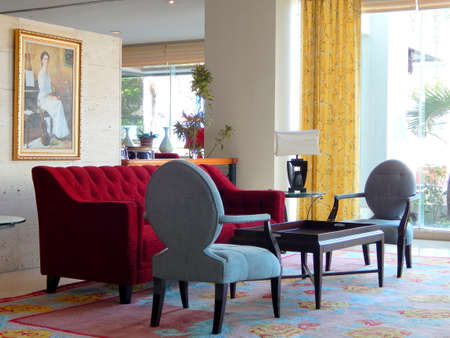 Manado, Indonesia - March 23rd, 2015: A red long sofa, a table, two grey chairs, carpet and a painting hanging on wallのeditorial素材