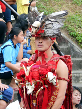Tomohon, Indonesia - April 29th, 2016; A man in a red traditional outfit of Minahasan, wearing a unique quill cap performing warrior dance of Kabasaran in a carnival parade on a sunny day.のeditorial素材