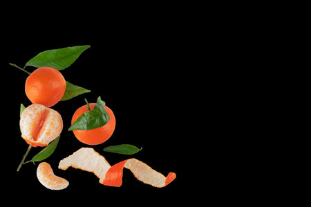 A few peeled and unpeeled fresh mandarins with green leafs on black backgroundの写真素材