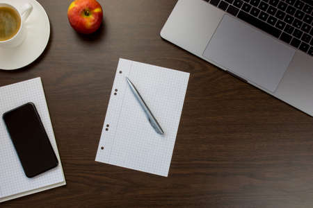Desk in the office with a notebook next to an apple and cup of coffee, a notepad and pen - wooden tableの写真素材