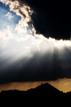 The sun shining through dark clouds on a house in the shadowの写真素材