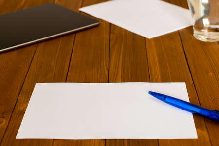 Workplace with a blank paper, blue pencil on a wooden table; tablet and a glass of water in the backの写真素材