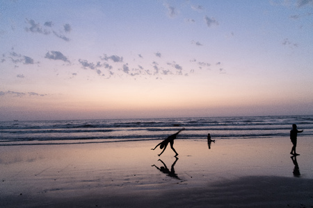 On a hot summer evening youth performs somersaults, flips  handstands at  beach. Silhouetted at dusk...