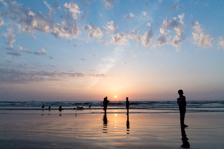 Silhouettes of  enjoying  beach  playing in  water. Setting sun  beautiful clouds in  background.の写真素材