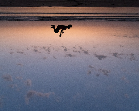 On a hot summer evening youth performs somersaults, flips  handstands at  beach. Silhouetted at dusk...