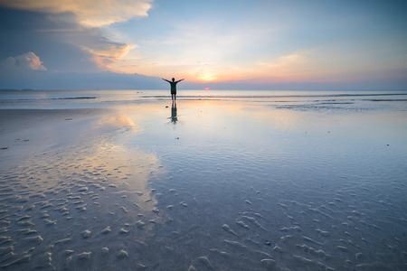 Silhouette of woman walking on the beach, along sea coast at sunset in the summerの写真素材