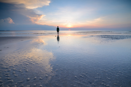 Silhouette of woman walking on the beach, along sea coast at sunset in the summerの写真素材