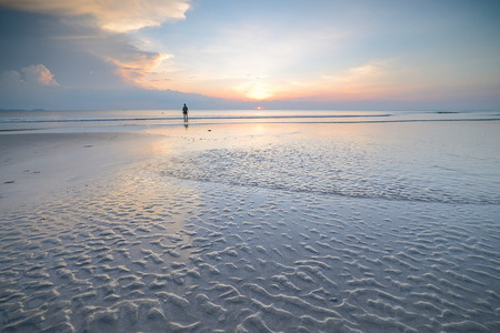 Silhouette of woman walking on the beach, along sea coast at sunset in the summerの写真素材