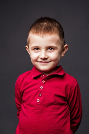 Closeup portrait of a cute little boy with hands behind his back against gray backgroundの写真素材