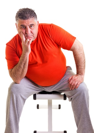 Overweight man sitting on a bench for abdominals, he takes a break, isolated on white backgroundの写真素材