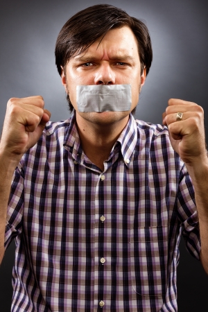  Angry  young man with duct tape over his mouth against gray background. Conceptual imageの写真素材
