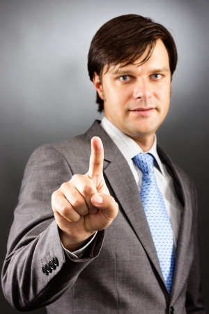 Businessman pressing an imaginary button against gray backgroundの写真素材