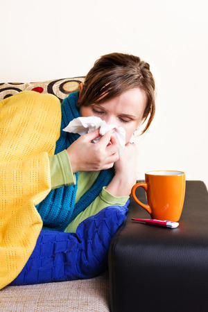 Young woman at home having flu, blowing her nose の写真素材