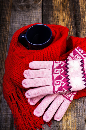 Cup of hot drink wrapped by red scarf and gloves on wooden board.Closeupの写真素材