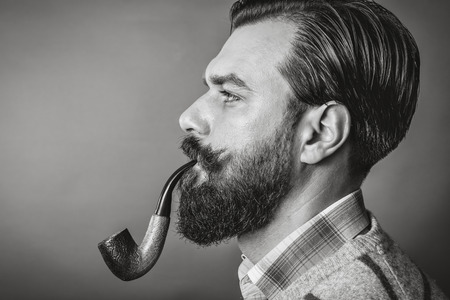 Studio shot of a handsome young man with retro look smoking pipe over gray backgroundの写真素材