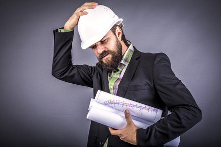 Overwhelmed businessman with hardhat over gray backgroundの写真素材