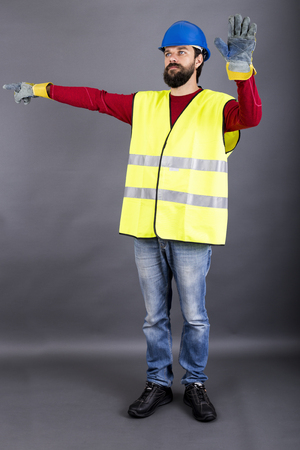 Young construction worker with hardhat directing traffic, showing  stop sign over gray backgroundの写真素材