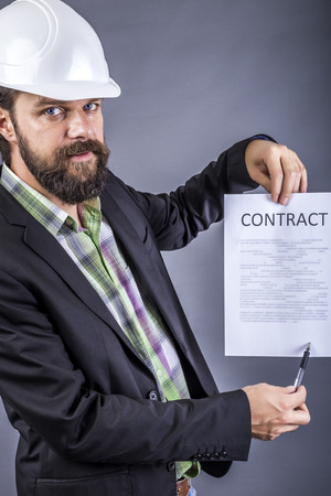 Portrait of young engineer with hardhat holding a contract over gray backgroundの写真素材