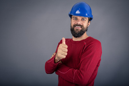 Happy young worker with hardhat showing ok sign over gray backgroundの写真素材
