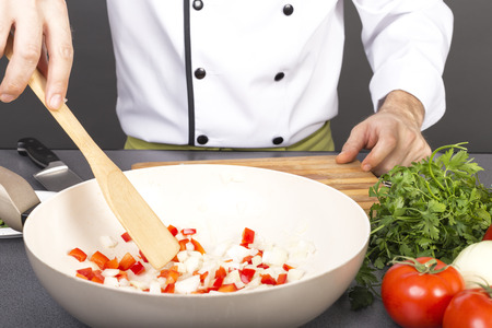 Chef mixing fresh vegetables in pan with a wooden spoon on grayの写真素材