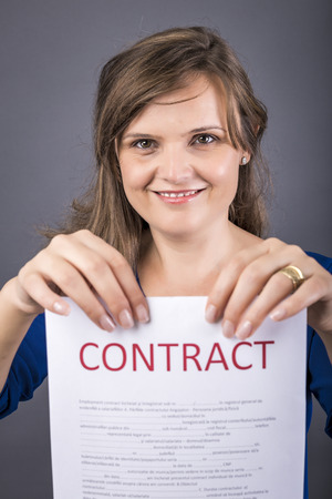 Portrait of young happy woman holding a contract over gray backgroundの写真素材