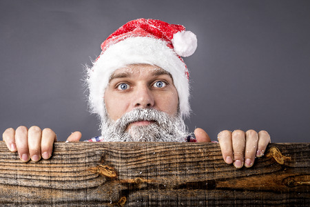 Closeup of a  scared man with frozen beard and moustache wearing red santa claus  over gray backgroundの写真素材