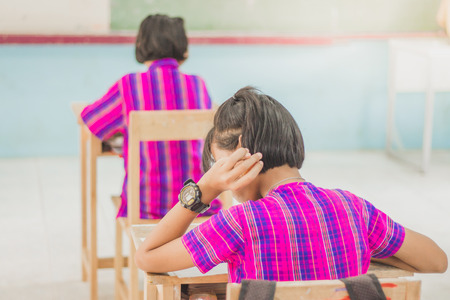 Back view abstract background of examination room with students  in uniform sitting on lecture chair doing final exam or study in classroom.の写真素材