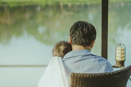 Dad and son  waiting for mom on the waterfront balcony in the morning at homeの写真素材