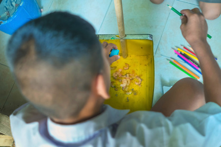 Elementary student sharpen the color pencil into the dustpan in front of classroomの写真素材