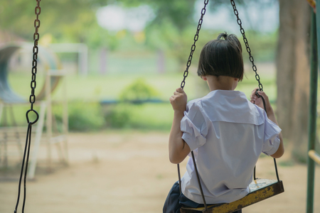 Back view of young girl sit on swing for wait her friend at the playground.の写真素材