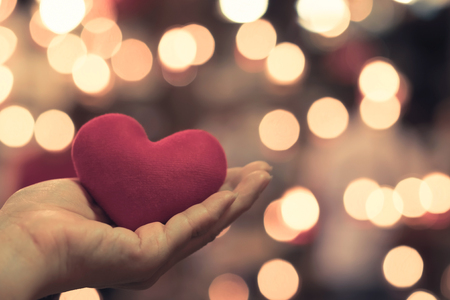 Hand hold red heart shape pillow with beautiful bokeh by candle light. Love concept on Valentine day.の写真素材