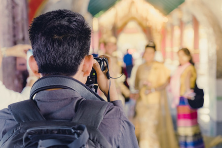 Myanmar wedding photography. A Burmese couple in a tradition dress that was photographed by a wedding photographer and his assistant in a famous temple. Villagers believe this brings good luck to young couples. Selective focus on photographer assistant.の写真素材