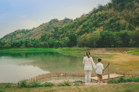 Back view of Mom and son are resting and taking care of their ducks in the eveningの写真素材