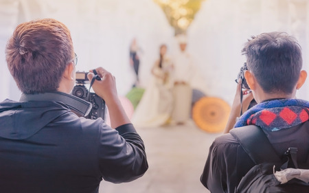 Myanmar wedding photography. A Burmese couple in a tradition dress that was photographed by a wedding photographer and his assistant in a famous temple. Villagers believe this brings good luck to young couples. Selective focus on photographer assistant.の写真素材
